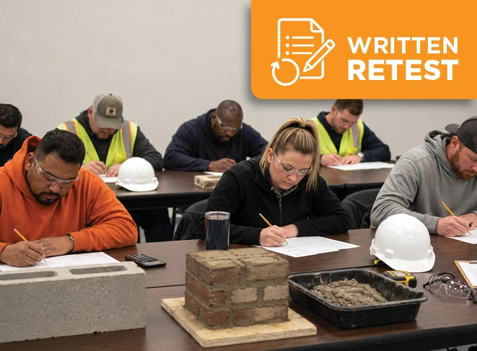 Masonry field testing candidates taking a written retest in a classroom with masonry units, mortar samples, and testing tools on the table.