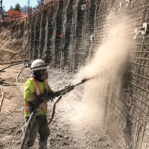Shotcreter applying dry-mix shotcrete to a reinforced wall at a construction site.